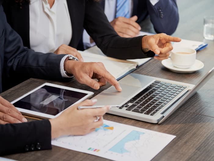 Hands on a table with a laptop, a tablet and printed charts